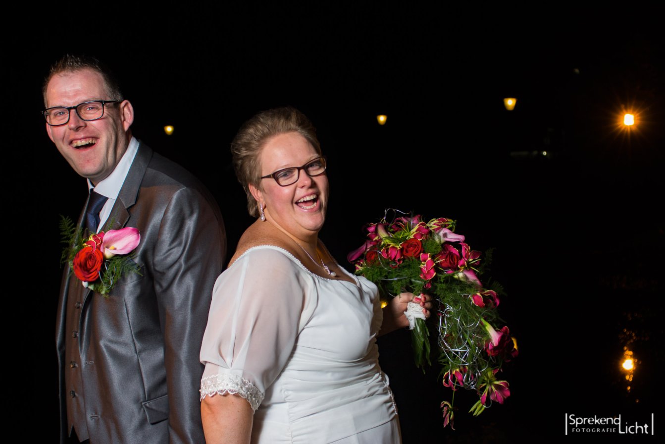 Lachend bruidspaar rug aan rug in de avond